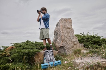 photography and nature concept, indian backpacker taking shot on digital camera and standing on rock