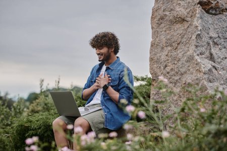 digital nomad concept, joyful indian freelancer having video call on laptop in natural location
