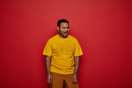 Photo for Cheerful indian man in bright casual attire posing with opened mouth on red background in studio - Royalty Free Image