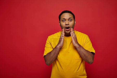 Photo for Shocked indian man in bright casual clothes looking at camera on red background, open mouth - Royalty Free Image
