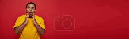shocked indian man in bright casual clothes looking at camera on red background, open mouth, banner