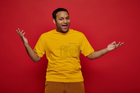emotionaler indischer Mann in heller Freizeitkleidung gestikuliert und redet auf rotem Hintergrund im Studio