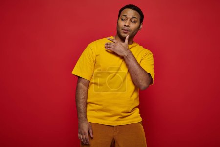 self-confidant haughty indian man in bright casual clothes grimacing on red background in studio