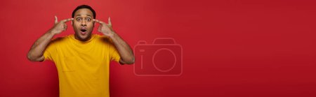 Photo for Mind blowing, shocked indian man with fingers near head looking at camera on red backdrop, banner - Royalty Free Image