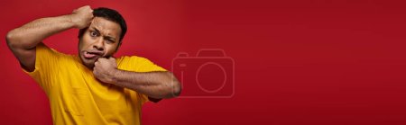 face expression, indian man in yellow t-shirt punching himself into face on red backdrop, banner