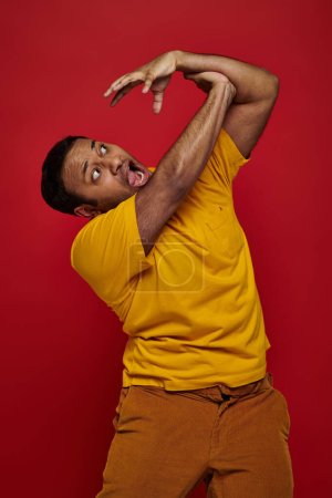 face expression, hand on shocked indian man in yellow t-shirt attacking him on red background