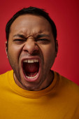 face expression, emotional indian man in yellow t-shirt screaming on red background, open mouth magic mug #670405376