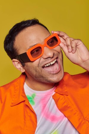 Selbstausdruckskonzept, aufgeregter indischer Mann mit leuchtend oranger Sonnenbrille, der auf gelbem Hintergrund lächelt