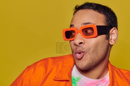 Selbstausdruckskonzept, überraschter indischer Mann mit orangefarbener Sonnenbrille, der vor gelbem Hintergrund wegschaut