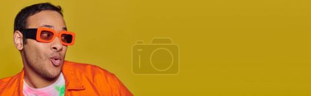 Foto de Concepto de expresión personal, hombre indio sorprendido en gafas de sol naranjas sobre fondo amarillo, pancarta - Imagen libre de derechos