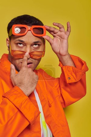 arrogant and confident indian man trying on different trendy sunglasses on yellow backdrop