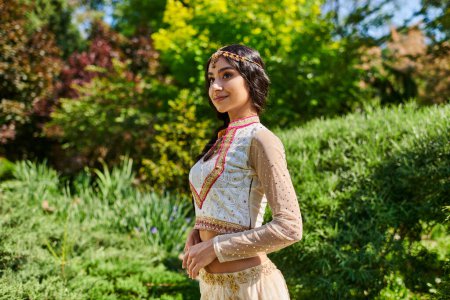 mujer india alegre en traje tradicional mirando hacia otro lado en el parque de verano