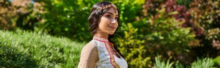 Téléchargez les photos : Parc d'été, femme indienne heureuse dans des vêtements authentiques élégants près de plantes vertes, bannière - en image libre de droit