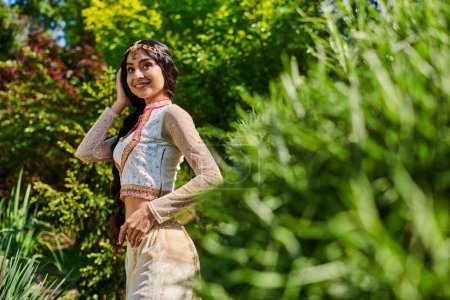 junge Indianerin in traditioneller Kleidung lächelt im Sommerpark auf verschwommenem Vordergrund