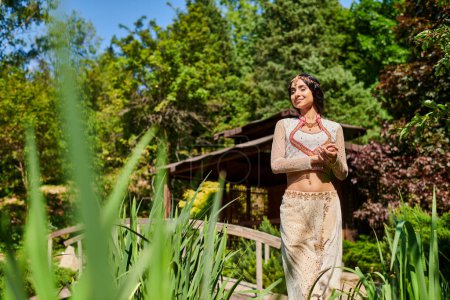 glückliche Indianerin in authentischer Kleidung steht mit geschlossenen Augen auf Holzbrücke im Park