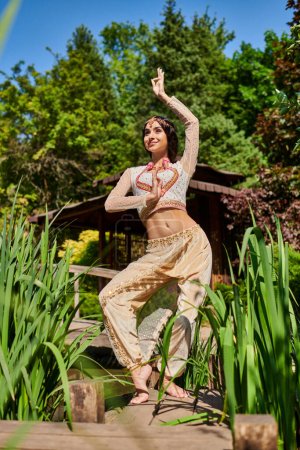 mujer india despreocupada y elegante en traje étnico bailando en el parque de verano en un día soleado