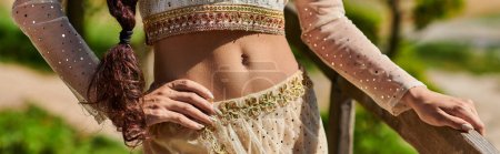 vue recadrée de la femme indienne en tenue authentique debout avec la main sur la hanche, parc d'été, bannière