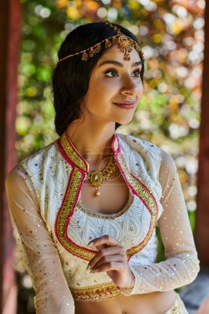 traditional fashion, portrait of young indian woman smiling and looking away in summer park