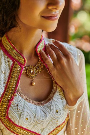 recortado vista de la mujer india sonriente en traje tradicional y collar de joyas posando al aire libre