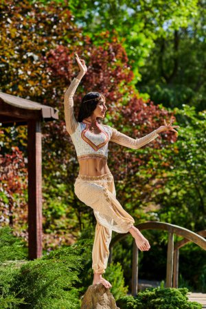 Foto de Parque de verano, mujer india con estilo en la ropa tradicional bailando en el día soleado, movimientos tradicionales - Imagen libre de derechos