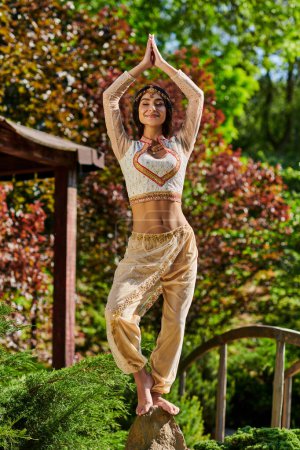 Foto de Mujer india alegre en ropa étnica elegante de pie con las manos de oración levantadas, felicidad de verano - Imagen libre de derechos