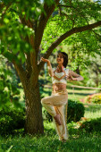 happy indian woman in elegant authentic attire dancing under tree on green lawn, summer sunny park hoodie #671993616