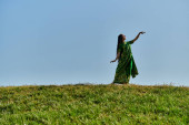 authenticity, enjoyment, happy indian woman in sari on green meadow under blue sky, summer day t-shirt #671993678
