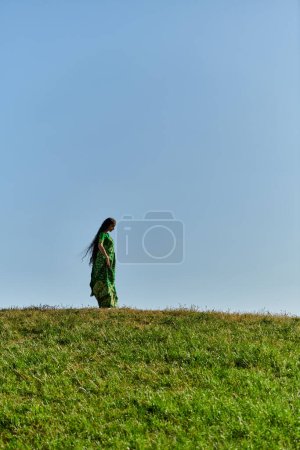 summer, ethnic heritage, young indian woman under blue cloudless sky in green field