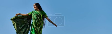 loisirs d'été, femme indienne en sari souriant et regardant loin sous le ciel bleu sans nuages, bannière