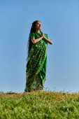 happy indian woman in sari with praying hands and closed eyes on lawn under blue sky, summer day Poster #671993846