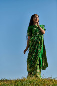 young indian woman in elegant traditional sari in green field under blue sky, summer happiness mug #671993864