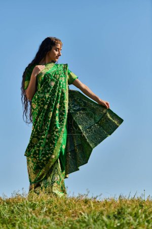 kulturelles Erbe, Indianerin im traditionellen Sari auf einer grünen Wiese unter blauem Sommerhimmel