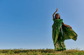 summer dance of smiling indian woman in authentic sari in green field under blue sky t-shirt #671993892