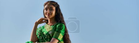 Photo for Smiling young indian woman in traditional sari posing with blue sky on background outdoors, banner - Royalty Free Image