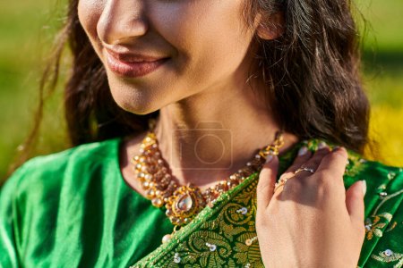 cropped view of smiling young woman in green sari posing and standing outdoors