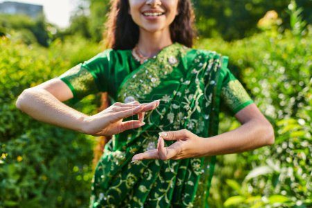 cropped view of young smiling woman in sari gesturing and standing in blurred park