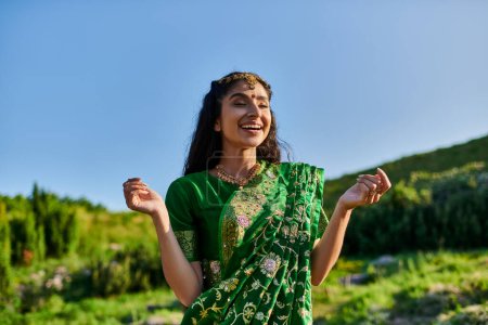 glückliche junge Indianerin in stylischem Sari posiert und mit Landschaft im Hintergrund steht