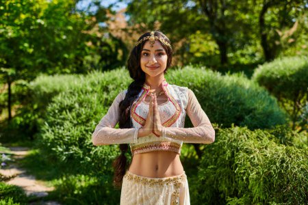 lächelnde und stylische indische Frau in Matha Patti bei der Geste der betenden Hände im Park