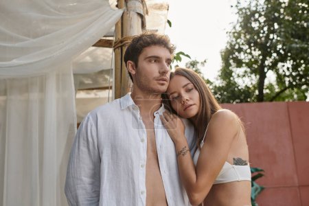 mujer tatuada apoyada en el hombro del novio en camisa blanca durante las vacaciones de verano, romance