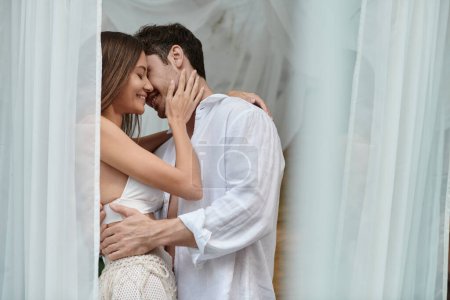 happy couple before kiss, handsome man embracing woman near white tulle of private pavilion