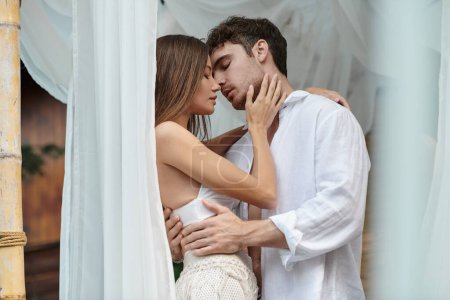 tender couple before kiss, handsome man embracing woman near white tulle of private pavilion