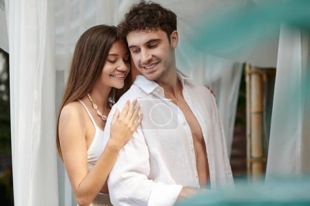 glückliches Paar, fröhliche Frau umarmt Mann in weißen Kleidern und lächelt im Sommerurlaub