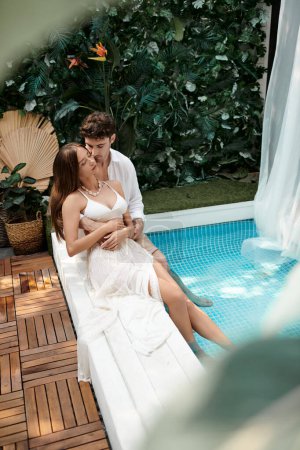 Paar in weißen Kleidern sitzt zusammen in der Nähe des Swimmingpools im Urlaub, romantisches Wochenende