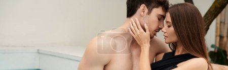 namiętna kobieta w stroju kąpielowym dotykająca twarzy mężczyzny bez koszuli z zamkniętymi oczami, przed całusowym transparentem