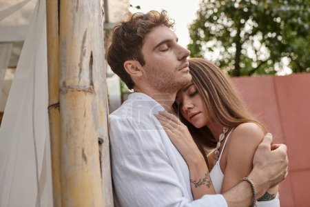 Téléchargez les photos : Moment romantique, bel homme embrassant belle femme près du pavillon de la plage pendant les vacances - en image libre de droit