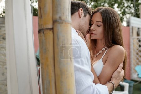 momento romántico, hombre guapo en camisa blanca abrazando y besando a la mujer con tatuaje durante las vacaciones