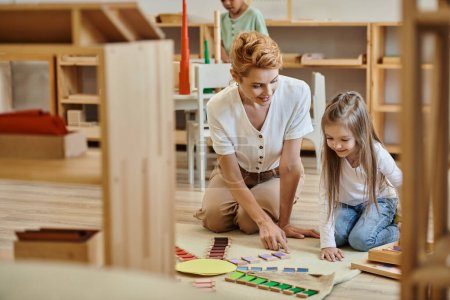 Montessori-Material, glückliches Mädchen spielt Lernspiel mit blonder Lehrerin, frühe Schulbildung
