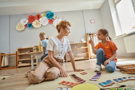 juego de combinación de colores, chica mostrando pieza de material montessori a la maestra feliz, educativo