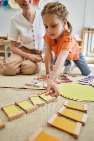 Photo for Montessori material, cute girl playing color matching game near female teacher, sitting on floor - Royalty Free Image