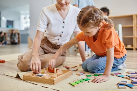 Foto de Montessori concepto de la escuela, chica jugando juego de combinación de colores cerca de profesor femenino, sentado en el suelo - Imagen libre de derechos